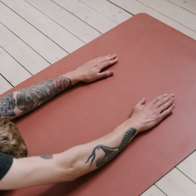 Ženska s tatuji izvaja jogo na joga podlogi